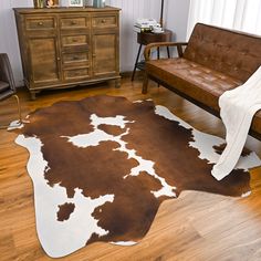 a brown and white cowhide rug in a living room with wood floors, leather couches and dresser