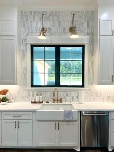 a kitchen with white cabinets and stainless steel dishwasher in front of two windows