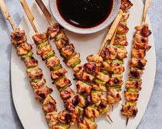 several skewers of chicken and vegetables on a plate with dipping sauce in a bowl