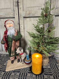 a small christmas tree next to an old fashioned doll and a candle on a rug