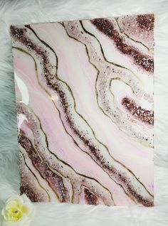 a pink and gold marble wall hanging on a white furnishing next to a flower