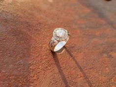 a diamond ring sitting on top of a red rock with the shadow of a person standing next to it