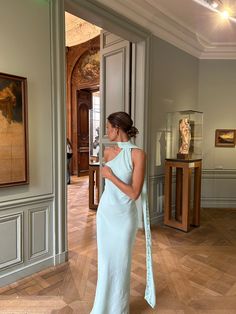 a woman in a blue dress is looking at some art on the wall behind her