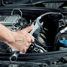 a man holding a wrench in front of a car engine