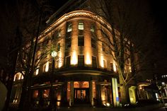 an old building lit up at night with lights on the windows and trees in front