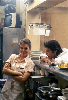 two people standing in a kitchen next to each other with plates on the counter behind them