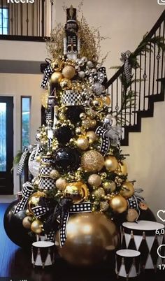 a christmas tree decorated with black and gold ornaments in a living room next to stairs