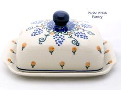 a white and blue dish with orange flowers on it's lid, sitting on a white surface