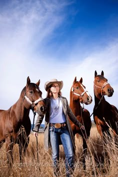 a woman is standing with three horses in a field