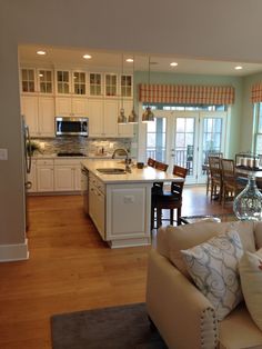 a living room and kitchen area in a home with hardwood floors, white cabinets, and an island