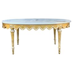 an oval marble top table with gold trimmings and scalloped legs,