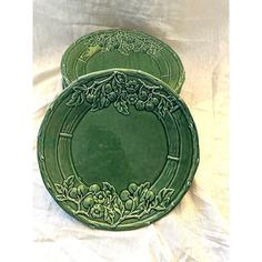 three green plates sitting on top of a white cloth covered tablecloth with flowers and leaves