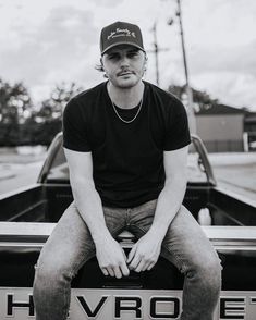 a man sitting on the hood of a car with his hands in his pockets and looking at the camera