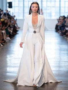 a model walks down the runway in a white gown with long sleeves and high slits