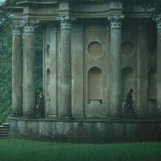 two people are standing in front of an old building with columns and arches on it