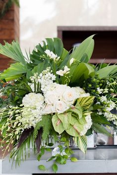 a vase filled with white flowers and greenery on top of a metal countertop