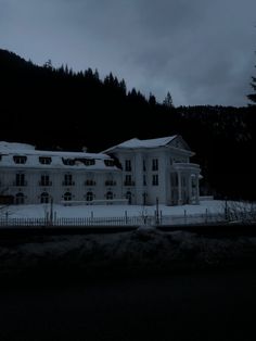 a large white house sitting on top of a snow covered hill next to a forest