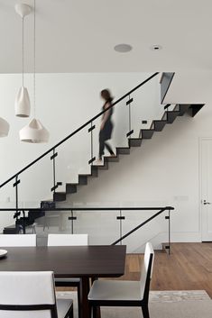 a woman is walking up the stairs in a house with white walls and wood floors