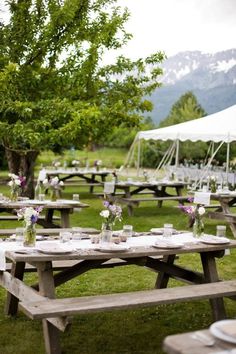 tables and chairs set up for an outdoor wedding reception in the grass with mountains in the background