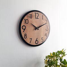 a wooden clock on the wall next to a potted plant and a white wall