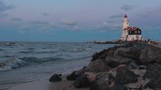 a light house sitting on top of a rocky beach next to the ocean at dusk