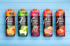 four bottles of fruit juice lined up against a blue background with oranges, kiwis and pomegranate