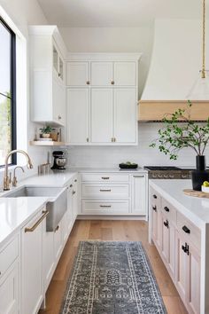 a kitchen with white cabinets and wood floors, an area rug in the middle of the floor