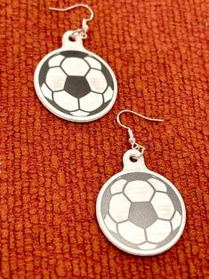 two silver earrings with soccer balls on them sitting on a red cloth covered tablecloth