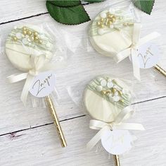 three white and gold candy lollipops with name tags on them sitting next to some green leaves