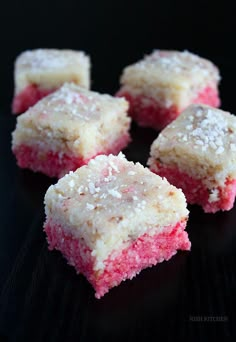 four pieces of pink and white cake on a black surface with powdered sugar sprinkled on top