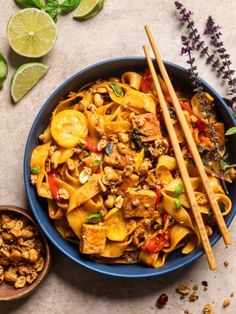 a bowl filled with noodles and vegetables next to chopsticks on top of a table