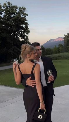 a man and woman standing next to each other holding wine glasses