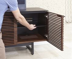 a man is opening the door to a small cabinet with shelves and drawers on both sides