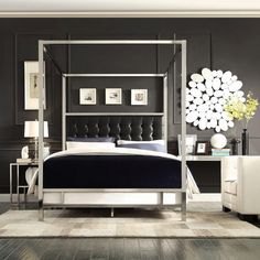 a bed with a black headboard and white sheets in a room that has gray walls