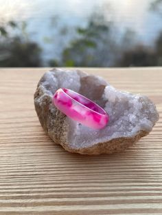 a pink ring sitting on top of a rock next to a wooden table with trees in the background