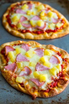 two pizzas with ham, pineapple and cheese on them sitting on a baking sheet