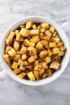 a white bowl filled with cooked potatoes on top of a marble counter