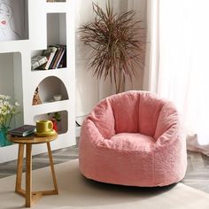 a pink chair sitting on top of a white floor next to a table and potted plant