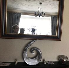 a mirror is hanging on the wall above a mantle with a sculpture in front of it