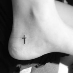 a small cross tattoo on the side of a person's foot is shown in black and white