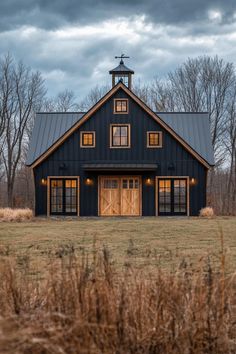 a large black barn with two windows and a steeple on top is lit up at night