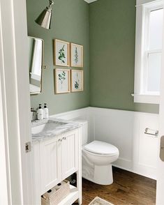 a white toilet sitting next to a sink in a bathroom under two pictures on the wall