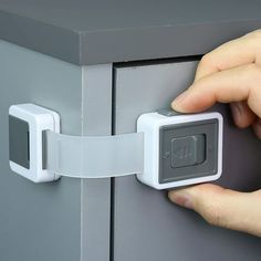 a person's hand is pulling the latch on a gray cabinet with white handles