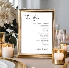 a table setting with candles, flowers and menu cards in gold frames on the table