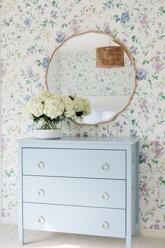 a blue dresser with flowers and a round mirror