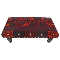 a red, blue and black ottoman with wheels on the bottom that has an intricate design