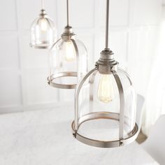 three light fixtures hanging from a kitchen island with marble counter tops and white tile walls