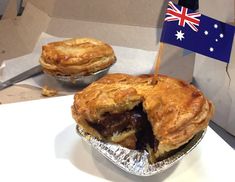 two pies sitting on top of tin foil with an australian flag sticking out of one