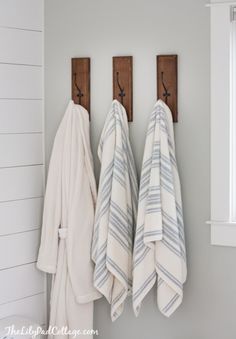 three towels hanging on the wall next to two wooden hooks