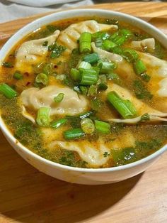 a white bowl filled with dumplings and green onions on top of a wooden cutting board